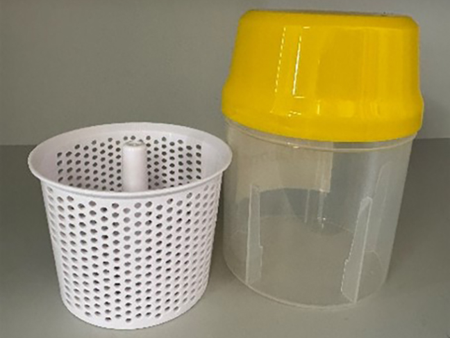Empty clear plastic cylindrical container with yellow lid, standing next to white plastic basket that fits inside container.