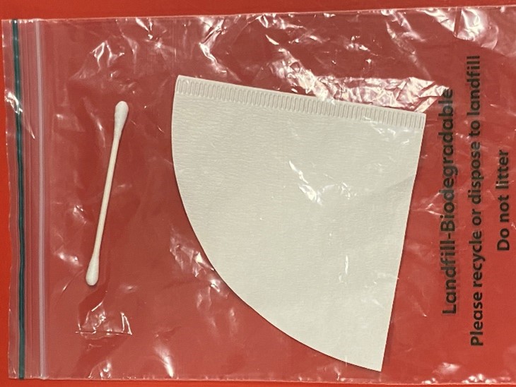 Image of a sample kit. Equipment includes sealable plastic bag and white cotton bud on red background.